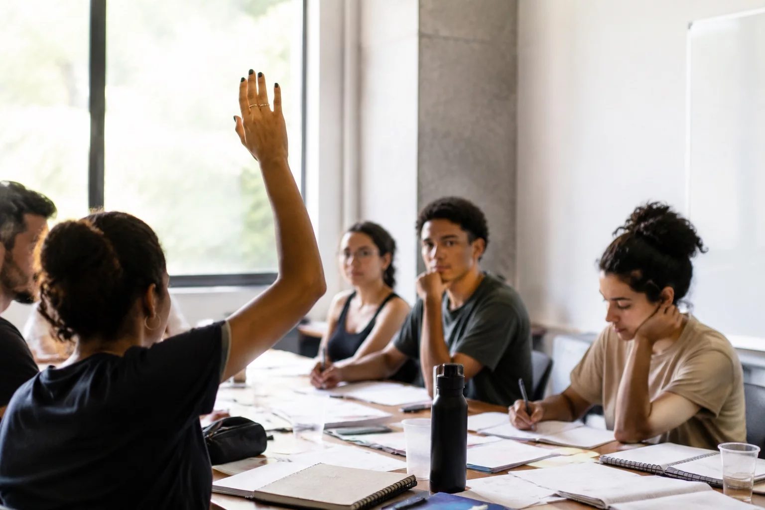 Estudante levantando a mão em uma mesa de seminário coberta de anotações